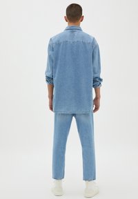 Camisa de mezclilla azul claro y pantalones a juego, con mangas largas y puños remangados, que presentan un ajuste relajado y un diseño de pierna recta.