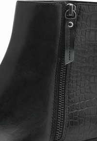 Bottines noires avec une tige en cuir lisse et des accents en faux crocodile texturé, dotées d'une fermeture éclair sur le côté.