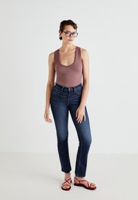 Geribbelde mauve tanktop, hoog uitgesneden donkerblauwe jeans en rode sandalen met bandjes. Het model heeft kort haar en rechthoekige bril.