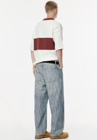 Tyk striktrøje i creme med en maroon horisontal stribe, parret med løse, lyseblå stribede denimjeans og brune støvler.