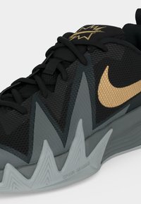 Black and gray athletic shoe with gold Nike swoosh, zigzag patterned sole, and black laces on a white background.