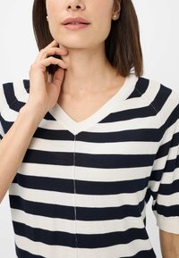 Marineblå og hvid stribet v-hals sweater med korte ærmer, der har en blød tekstur og en midtersteamsdetalje.