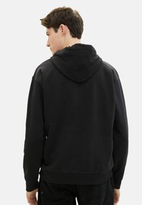 Hanorac negru fabricat dintr-un material moale, având o glugă mare, mâneci lungi și un elastic ajustat la talie. Textură netedă fără modele vizibile.