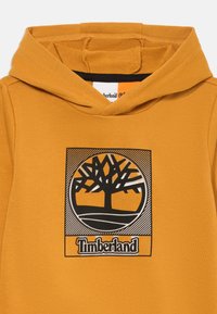 Narancssárga kapucnis pulóver fekete fa logóval és "Timberland" felirattal. Puha anyag, pulóver stílus, nagy kapucni és bordázott mandzsetta.