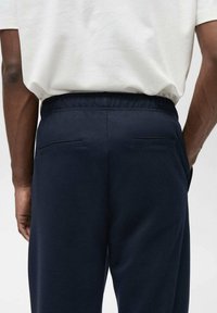 Mørkeblå sweatpants med elastisk linning og to flade baglommer. Materialet ser glat ud med en let glans.