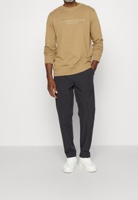 Sweat-shirt beige avec l'inscription "Copenhagen", assorti à un pantalon foncé et des baskets blanches. Le sweat-shirt présente un col rond et des poignets côtelés.