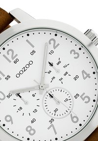 Silver case watch with a white dial, Arabic numerals, three hands, and a sub-dial. Brown leather strap. Clear day of the week markings.