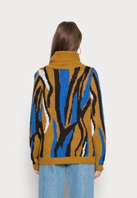 Sweter dziany z geometrycznym wzorem w kolorach brązowym, niebieskim, czarnym i białym, z wysokim kołnierzem i luźnym krojem. Miękka tekstura.