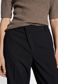 Black tailored trousers with a smooth texture, featuring a flat front design and discreet side pockets, complemented by a fitted ribbed brown top.