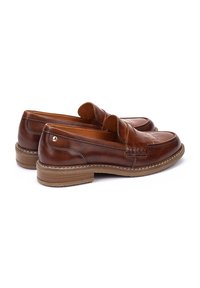 Mocasines de cuero marrón con un diseño bordado y acentos elevados. Presentan un tacón bajo apilado y una textura suave.