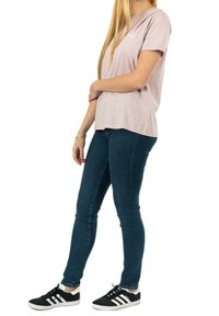 Světle růžové tričko s krátkým rukávem a kulatým výstřihem, v kombinaci s tmavě modrými skinny jeans a černými teniskami s bílými pruhy.
