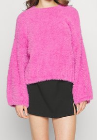 Fuzzy rosa tröja med rundad hals, långa ärmar och cropped nederkant, tillsammans med en svart kjol med sidofickor.