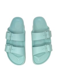 Un paio di sandali di gomma verde menta con due cinturini regolabili con fibbie e un plantare sagomato. Suola piatta, texture liscia.