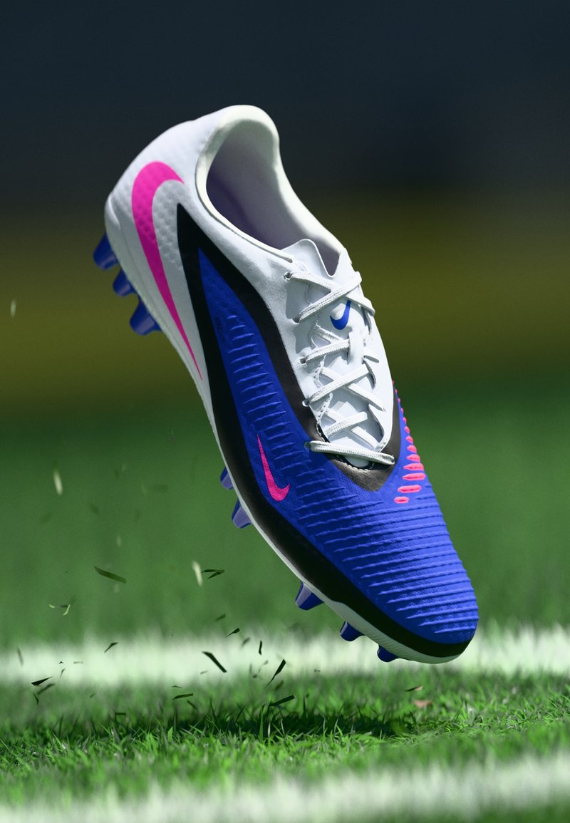 Ποδοσφαιρικό παπούτσι Nike με λευκό πάνω μέρος, μπλε και μαύρες πινελιές, υφή, ροζ λογότυπο και μωβ καρφιά, τοποθετημένο πάνω σε γρασίδι.