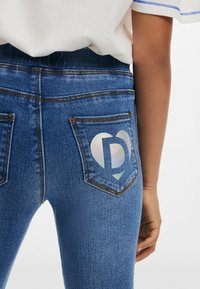 Hubené džíny v prostřední modři se subtilním vyblednutím. Výrazné světlé holografické srdíčko na zadní kapse. Klasický pětikipový design.