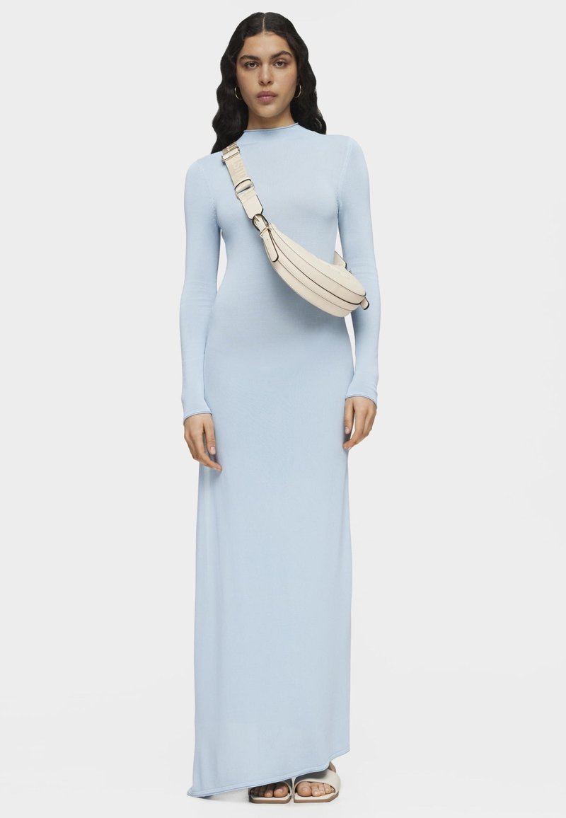 Jasnoniebieska, długosłodowa sukienka maxi z miękkiego materiału, zestawiona z kremową torebką na ramię o zaokrąglonym kształcie i regulowanym pasku.