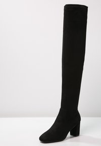 Botas negras por encima de la rodilla en suave ante, con un tacón cuadrado y un diseño de punta redonda. Textura suave y silueta ceñida.