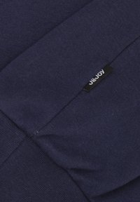Diepblauwe katoenen stof met een zachte textuur, voorzien van een zwart label met "J&Joy" in het wit. Het ontwerp omvat plooien en naden.