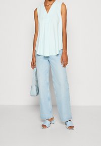 Haut sans manches bleu clair avec un col en V, associé à un jean large en denim clair et des sandales à talons carrés assorties bleu clair.