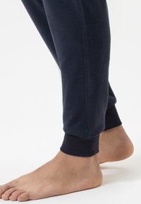 Mariene blauwe sweatpants gemaakt van zachte stof, met ribbels aan de mouwen en zijpanelen, met een blote voet zichtbaar ernaast.