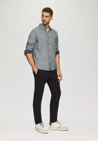 Grijze geruite button-up shirt, opgerolde mouwen, zwarte slim-fit broek en witte sneakers met lichte accenten. Simpel en casual ontwerp.