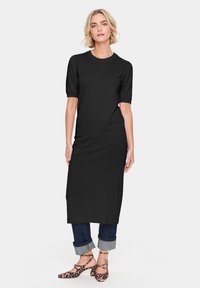 Robe noire côtelée longueur genoux avec des manches courtes, présentant un col rond. Portée avec un jean en denim foncé à revers et des talons en imprimé léopard.