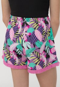 Pantaloni corti colorati con un motivo di foglie tropicali e fiori. Realizzati in materiale leggero, con un orlo frangiato rosa e una vita elasticizzata.