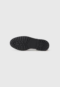 Suela de bota de goma negra con profundas ranuras para tracción, con una superficie lisa y una forma redondeada. Sin marcas visibles ni detalles adicionales.
