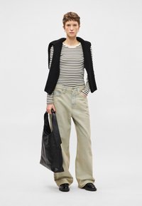 Ριγέ μακρυμάνικη μπλούζα, μαύρο γιλέκο, ανοιχτόχρωμα φαρδιά τζιν και μαύρη δερμάτινη τσάντα. Λείες υφές και χαλαρή εφαρμογή.