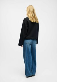 Sudadera negra recortada combinada con jeans de pierna ancha en azul. Tejido suave con una textura lisa, que presenta un ajuste relajado y un diseño sencillo.