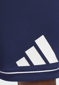 Pantalones cortos deportivos en navy con un tejido texturizado, que cuentan con un logotipo de tres rayas blancas en el dobladillo y una franja blanca de acento en la parte inferior.