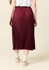 Burgundy veckad midikjol med elastisk midja, slät textur och en lätt sidoklyfta. Buren med vita strumpor och sneakers med metalliska detaljer.