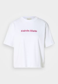 Balta kokvilnas T-krekls ar īsām piedurknēm un apaļu kakla izgriezumu, kurā priekšā sarkanos burtiem ir izšūts "Calvin Klein".