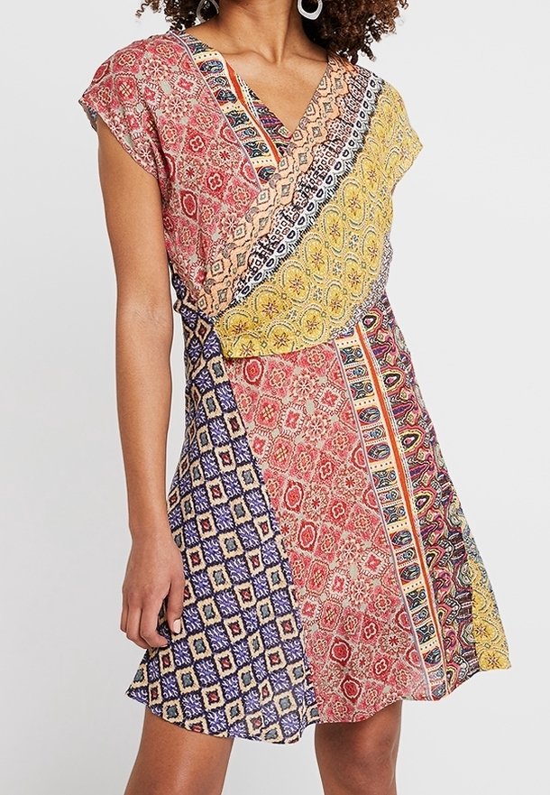 Femme portant une robe à patchwork multicolore avec des manches courtes et un décolleté en V sur un fond uni.