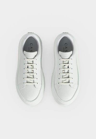 Paire de baskets en cuir blanc avec un design à lacets, bouts arrondis et marquage visible sur des semelles intérieures grises rembourrées, sur un fond uni.