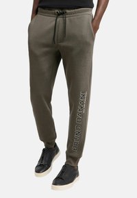 Olivgrüne Jogginghose mit schmaler Passform, mit Kordelzugbund und Seitentaschen; "Bruno Banani"-Logo vertikal in Weiß gedruckt.