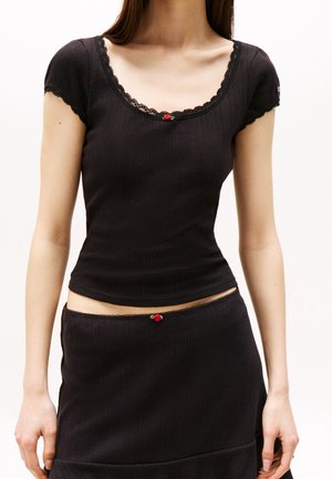 Haut noir ajusté avec des manches courtes, bordure en dentelle et un accent de fleur rouge au col. Texture côtelée, associé à une jupe assortie.