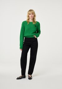 Groen wollen trui met een ronde hals, gecombineerd met zwarte wijde broekpijpen en zwarte spitse ballerina's. Minimalistisch ontwerp zonder patronen.