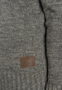 Grijze gebreide trui met geribbelde manchetten, voorzien van een leren label. De textuur is dik en het ontwerp is eenvoudig zonder patronen.