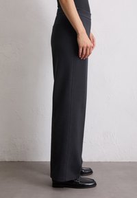Schwarz, weit geschnittene Hose aus weichem, dehnbarem Stoff mit hohem Bund und Seitentaschen. Glatte Textur mit klaren Linien.