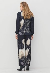 Afgedrukte zwarte outfit met een bloemenmotief in roomwit en grijs, met een relaxte top en wijde broekspijpen, gecombineerd met zwarte hoge hakken.