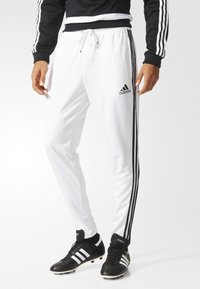 Vita sportbyxor med svart dragsko, med tre svarta ränder längs varje sida och en Adidas-logotyp på vänster lår.