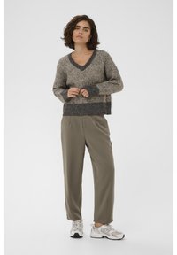 Pullover a V in maglia color beige e grigio con motivo testurizzato; abbinato a pantaloni verde oliva e sneakers grigio chiaro.