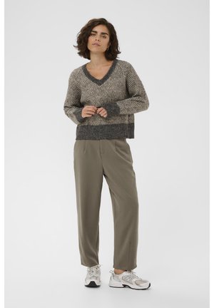 V-hals, gebreide trui in beige en grijs met een gestructureerd patroon; gecombineerd met olijfgroene broek en lichtgrijze sneakers.