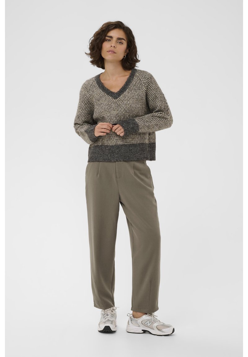 Pullover a V in maglia color beige e grigio con motivo testurizzato; abbinato a pantaloni verde oliva e sneakers grigio chiaro.