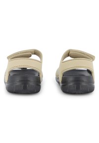 Μπεζ σανδάλια με υφή μαύρης σόλας, με δύο ρυθμιζόμενους ιμάντες στο πίσω μέρος και ανοιχτό σχεδιασμό για καλύτερο αερισμό.