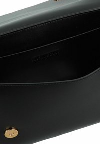 Borsa a mano nera in pelle con superficie liscia, chiusura a scatto in tonalità oro e logo impresso all'interno. Design minimalista con bordi morbidi.