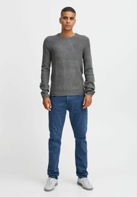 Pulover gri cu model texturat, cu guler rotund, asortat cu pantaloni blau cu tăietură slim. Ținuta este completată cu adidași gri.