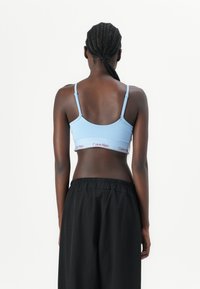 Lichtblauwe katoenen bralette met dunne bandjes en een elastische band met het "Calvin Klein" logo in het rood. Soepele textuur, afgerond ontwerp aan de achterkant.