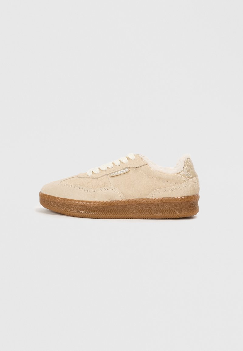 Beżowe zamszowe sneakersy z teksturowaną gumową podeszwą, kremowymi sznurówkami i futrzanym wykończeniem. Posiadają subtelną metkę z logo po boku.